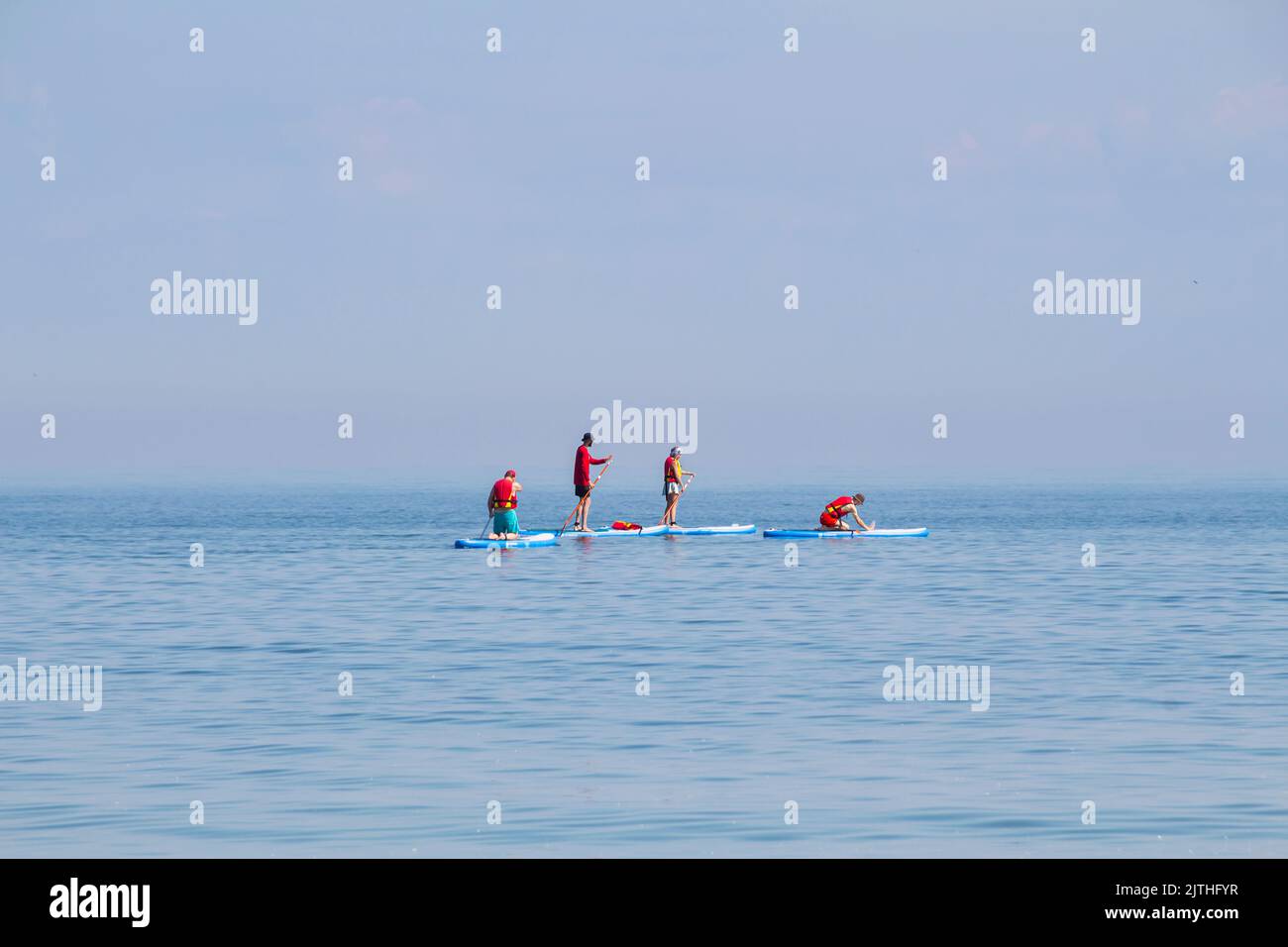 Aktive Familie auf SUP-Boards reiten und an einem schönen Morgen im Meer paddeln, Kopierplatz, selektiver Fokus. Familienurlaubsreisekonzept, Sommerurlaub Stockfoto