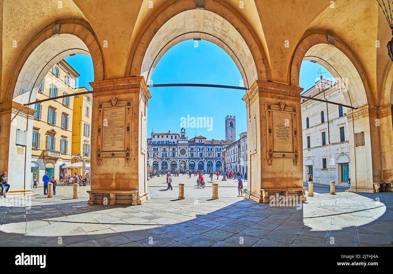 BRESCIA, ITALIEN - 10. APRIL 2022: Der belebte Fußgängerplatz Loggia aus dem Portikus des Palazzo della Loggia mit hohen Steinbögen, am 10. April Stockfoto