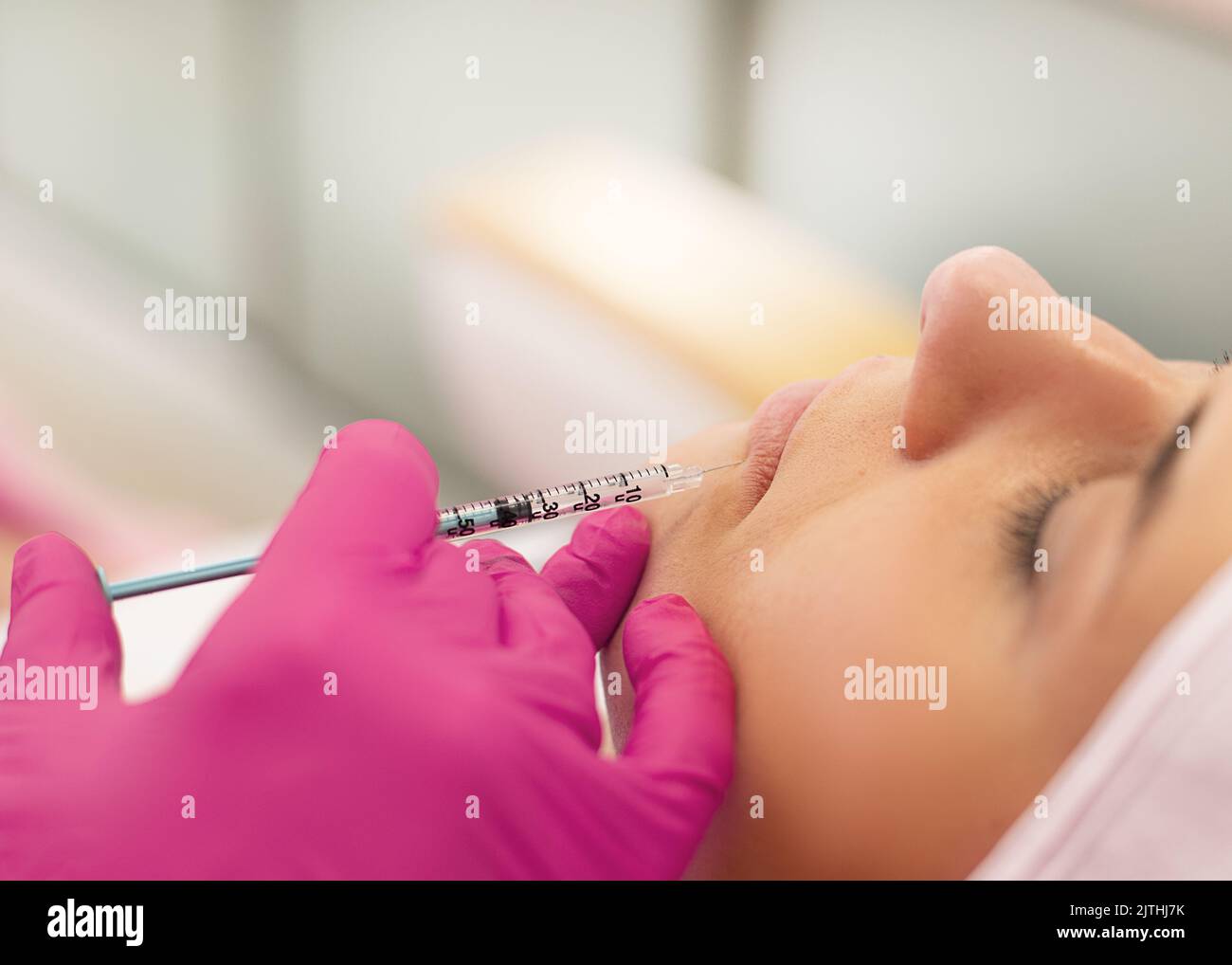 Nahaufnahme einer jungen Frau, die eine Schönheitsspritze in die Lippen bekommt. Kosmetologe machen Verfahren in rosa Handschuhe im Salon. Stockfoto