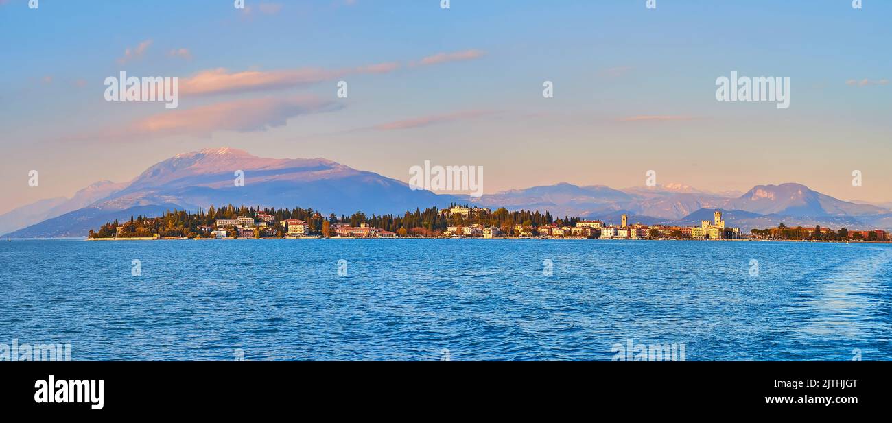 Panorama von gekräuselten azurblauen Gewässern des Gardasees mit landschaftlicher Skyline von Sirmione gegen die nebligen Garda Prealps bei Sonnenuntergang, Italien Stockfoto