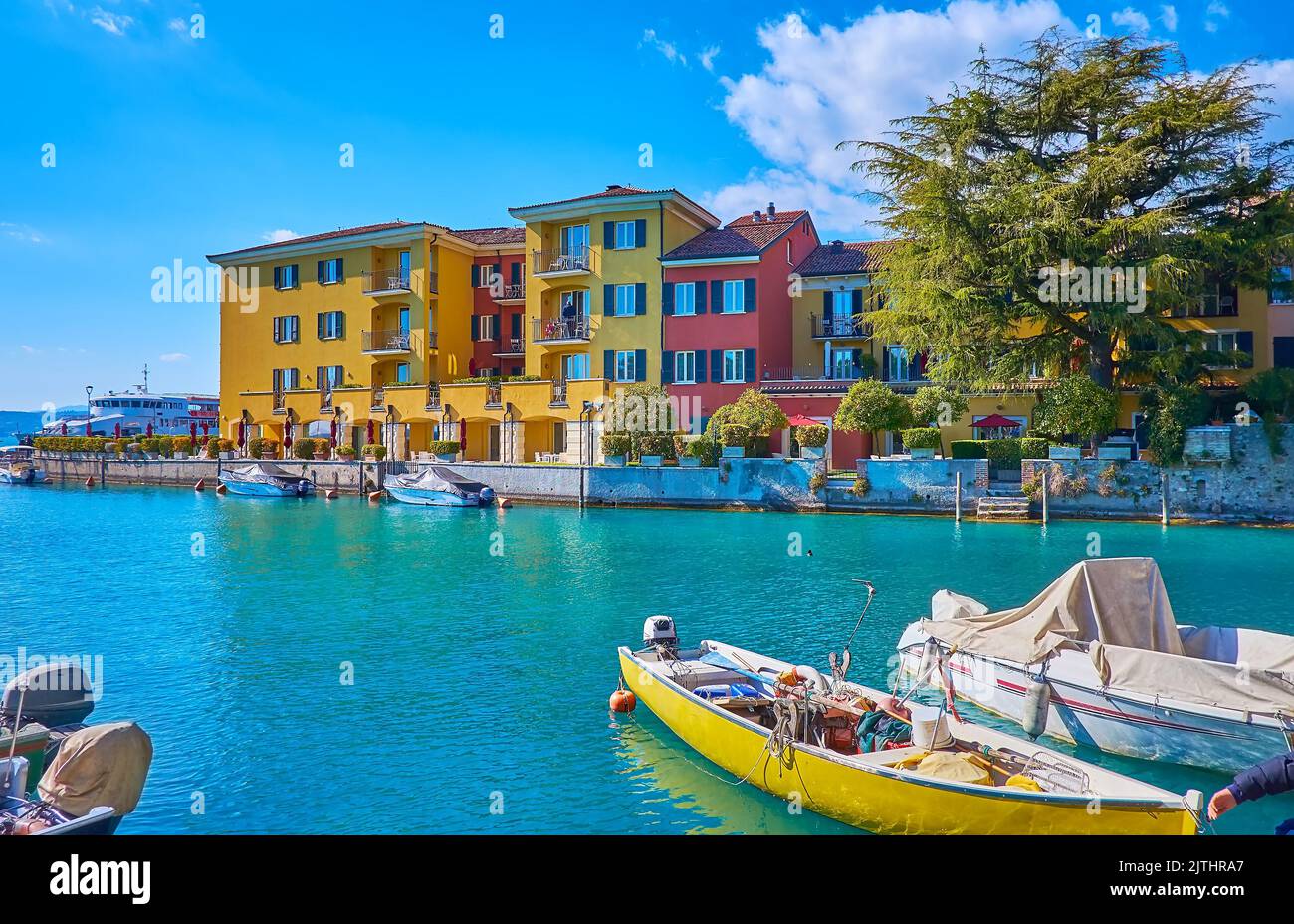 Die farbigen Fischer- und Touristenboote in der Marina von Sirmione, neben der Altstadt gelegen und gegenüber traditionellen Häusern und Villen, Lombardei, Italien Stockfoto