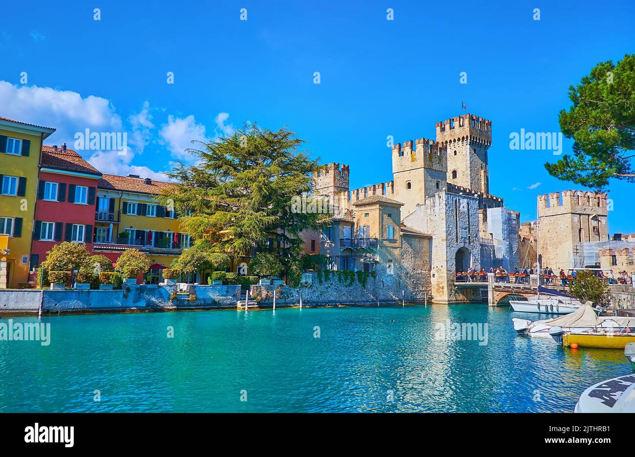 Der kleine Hafen von Sirmione Touristenort mit Blick auf schöne farbige Häuser, Hotels, Scaligero Castle und kleine Boote, die am Ufer, Lomba, vertäut Stockfoto