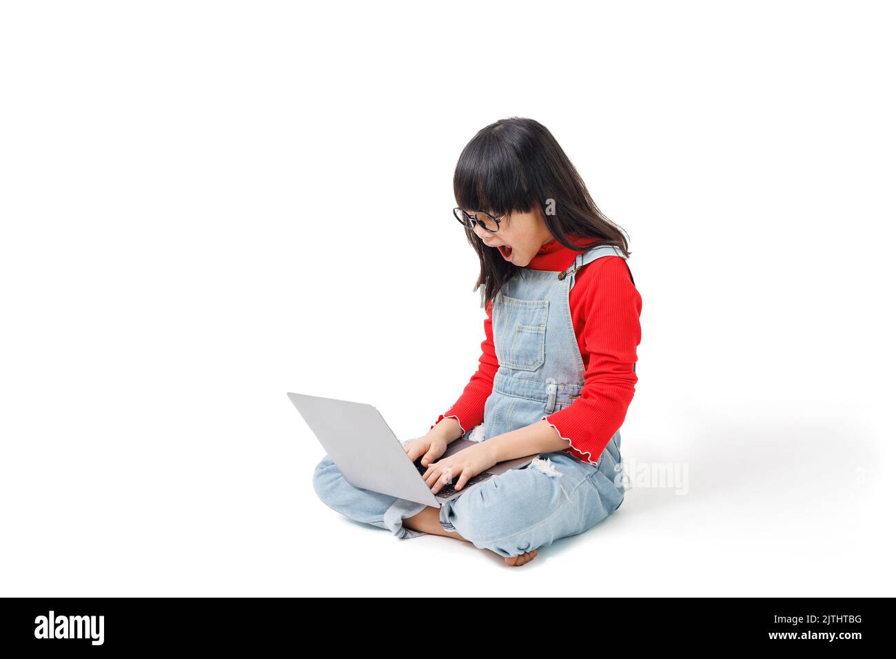 Ein junges Mädchen saß auf dem Boden, arbeitete an einem Computer, mit einem überraschenden Gesichtsausdruck. Stockfoto