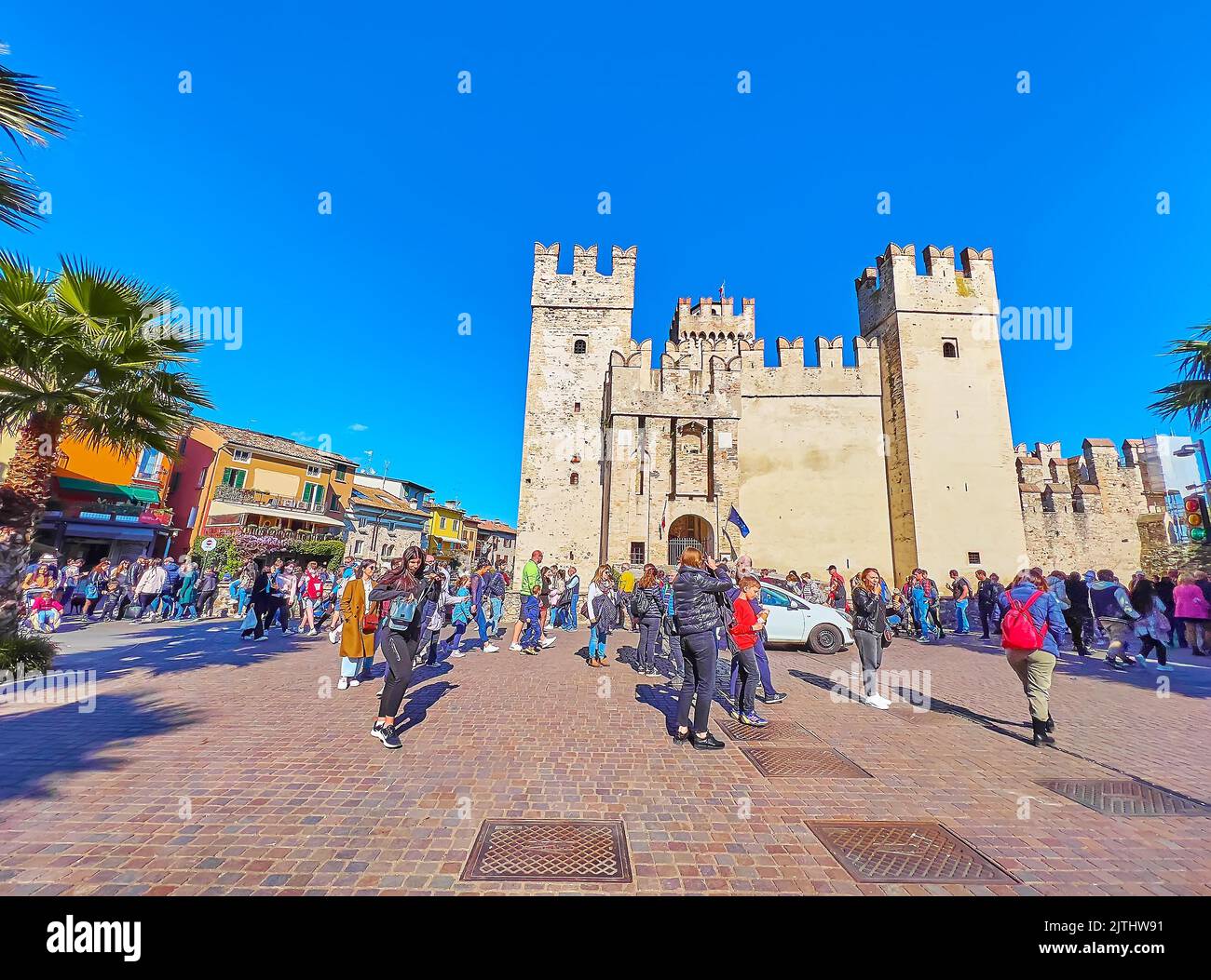 SIRMIONE, ITALIEN - 10. APRIL 2022: Der überfüllte Piazza Castello Platz mit alten Häusern, Restaurants im Freien und der historischen Burg Scaligero mit hohem Turm Stockfoto