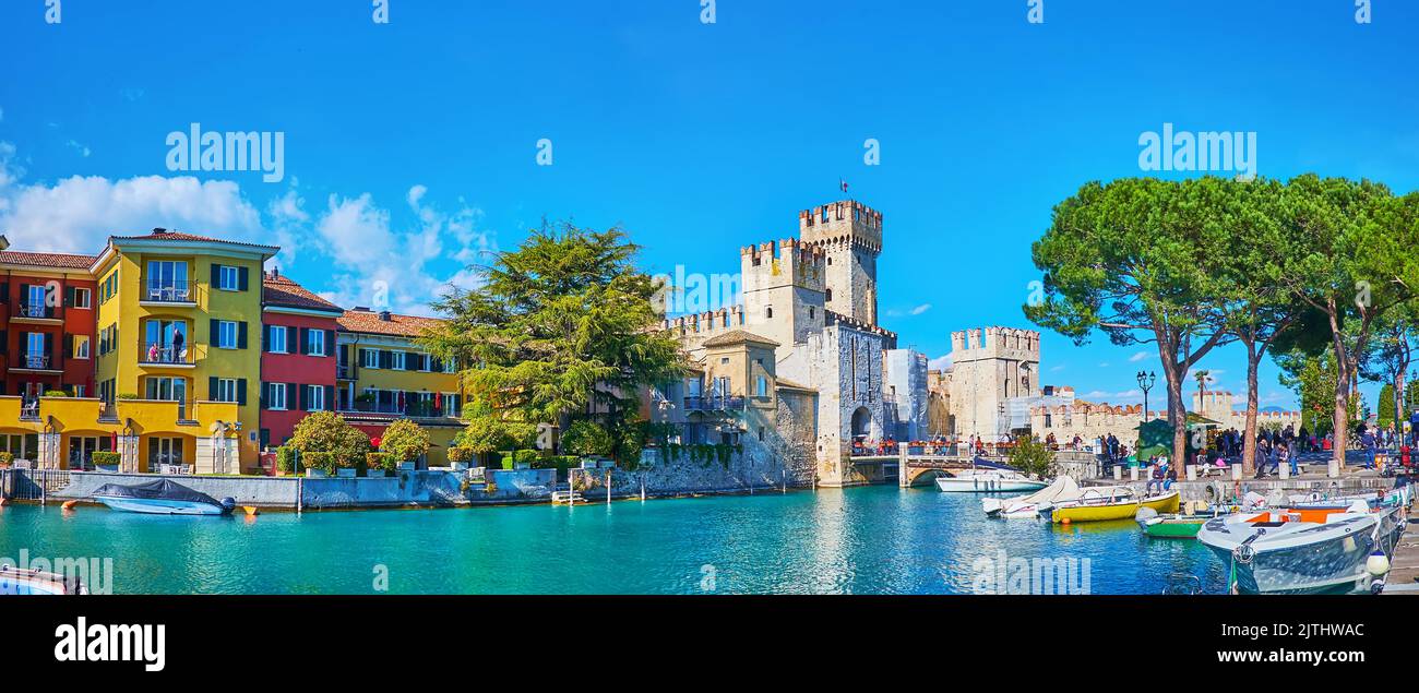Der malerische Yachthafen von Sirmione mit azurblauem Wasser des Gardasees, farbigen Häusern, Scaligero Castle und ausgebreiteten grünen Kiefern, Sirmione, Italien Stockfoto