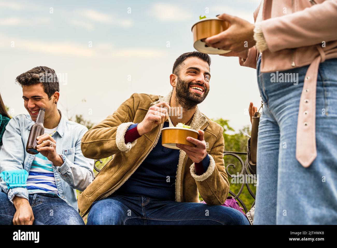 Fröhliche Freunde treffen sich zusammen, essen Essen zum Mitnehmen und sitzen am Wochenende im Freien - Menschen, Essen und Trinken Essen zum Mitnehmen Stockfoto