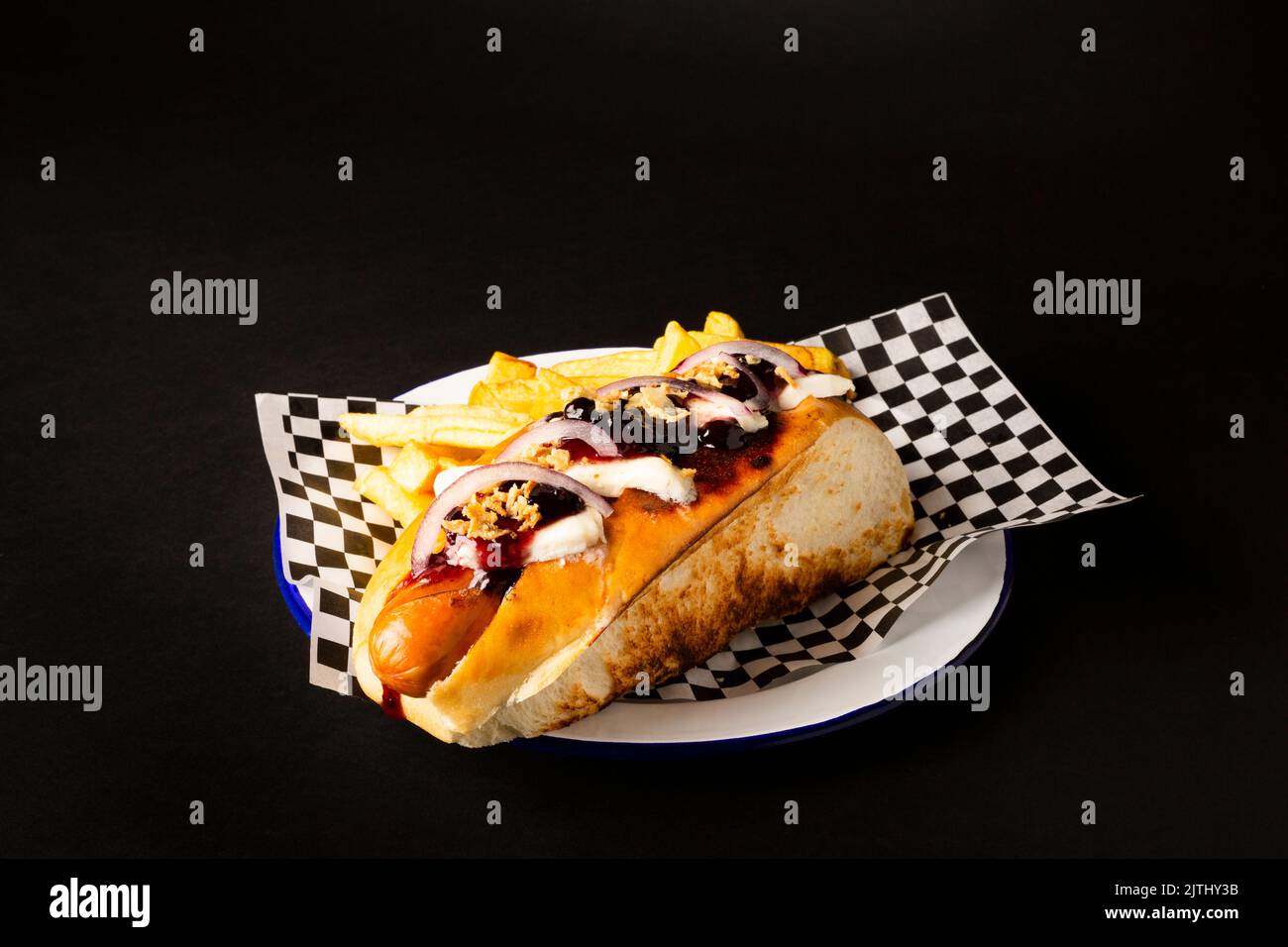 Frankfurter Wurst mit Zwiebel, Käse und pommes auf einem weißen Teller auf schwarzem Hintergrund Stockfoto