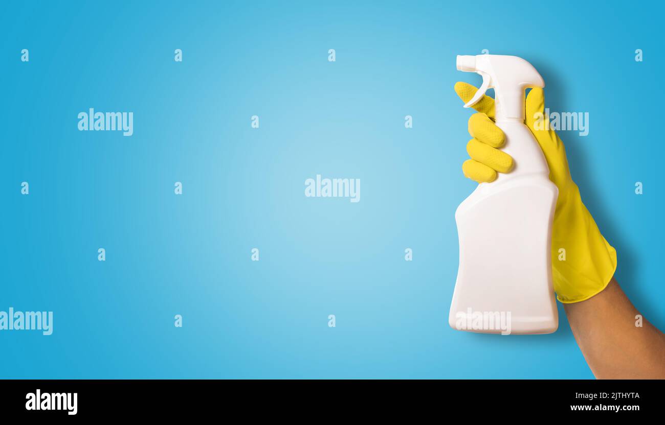 Hand in gelben Gummi-Handschuh hält weißen blanken Reinigungsspray-Flasche auf blauem Hintergrund. Copy Space Stockfoto