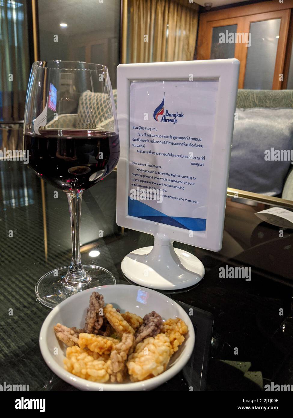 Ein Glas Rotwein und eine Schüssel Snacks auf einem Tisch in der Bangkok Airways Business Lounge des Bangkok International Airport, Thailand Stockfoto