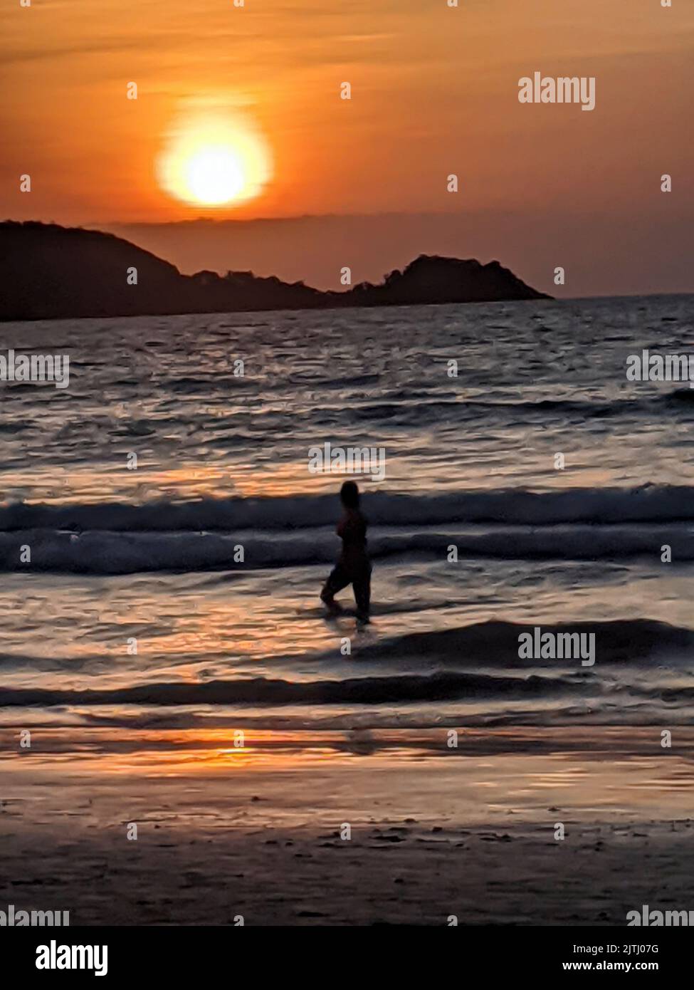 Die Person wird vor dem Sonnenuntergang geschildet, als sie am Strand von Kata Beach, Phuket, Thailand, entlang geht. Stockfoto