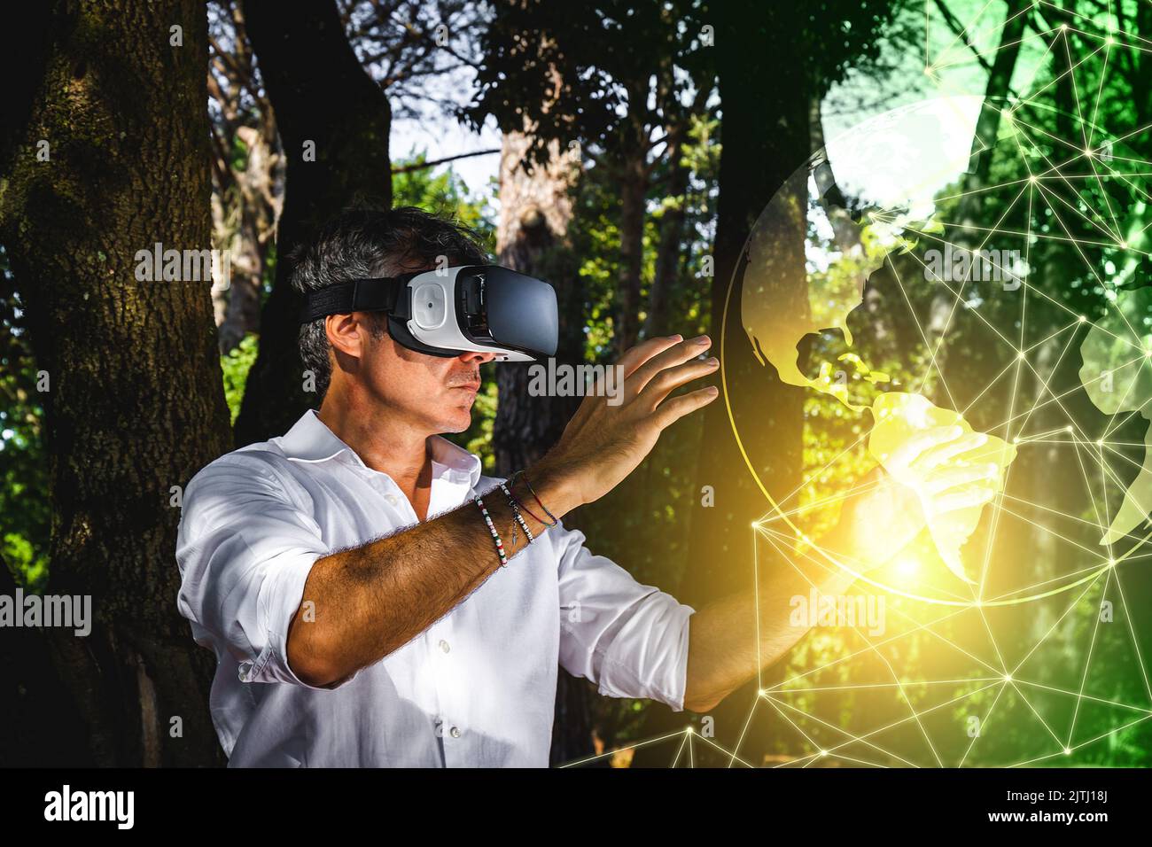 Der junge Mann nutzt einen Virtual-Reality-Betrachter im Park. Der gutaussehende Geschäftsmann arbeitet mit einem Virtual-Reality-Betrachter im Freien. Stockfoto