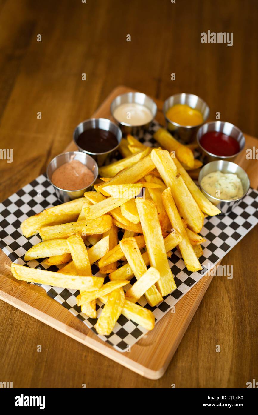 Pommes frites auf einem Holztisch, begleitet von verschiedenen Saucen auf einem Holztisch Stockfoto