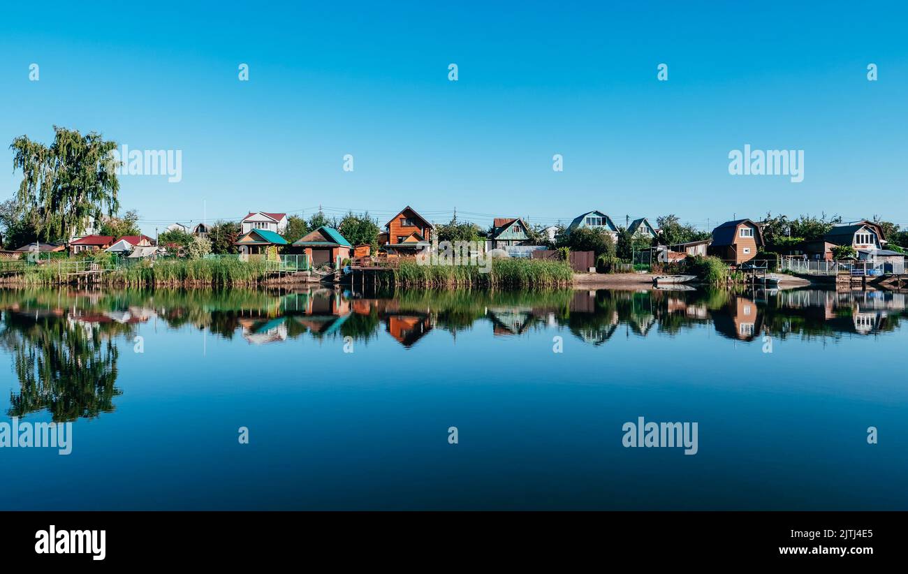 Landhäuser am Ufer des Flusses. Spiegelung von Häusern im Wasser. Wunderschöne Sommerlandschaft Stockfoto