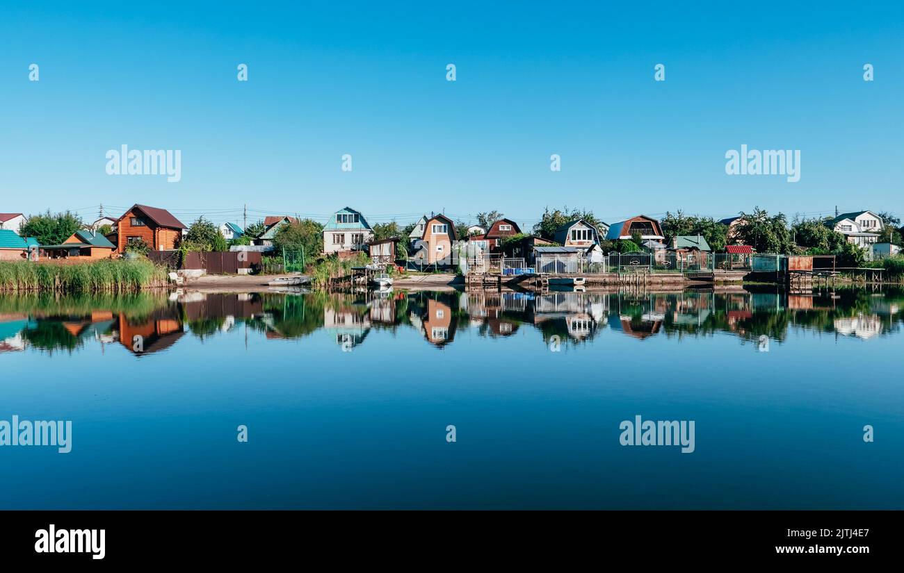 Landhäuser am Ufer des Flusses. Spiegelung von Häusern im Wasser. Wunderschöne Sommerlandschaft Stockfoto