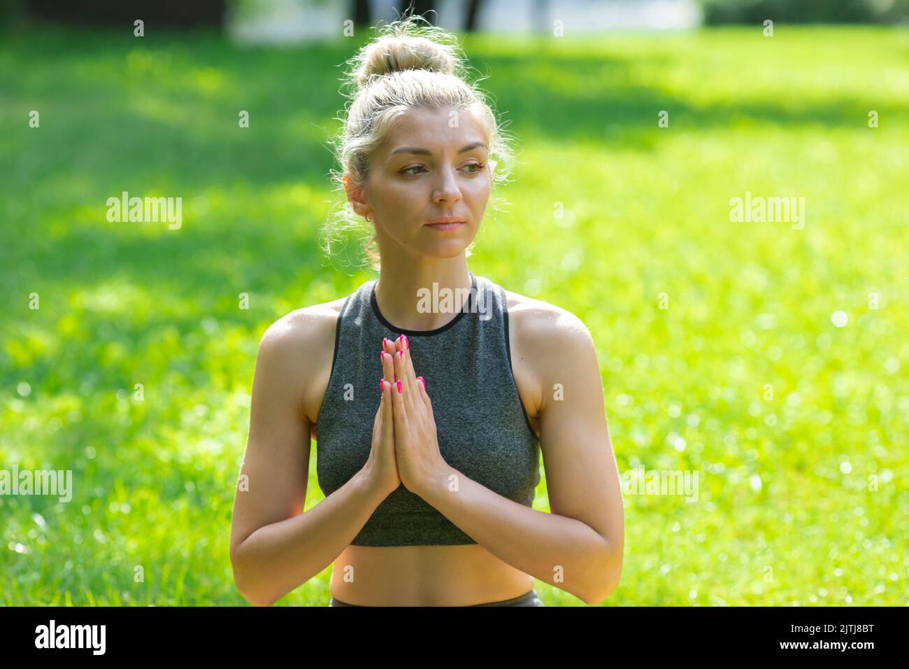 Eine Frau, die im Sommer im Park auf dem grünen Gras sitzt, hat ihre Handflächen zusammengelegt Stockfoto