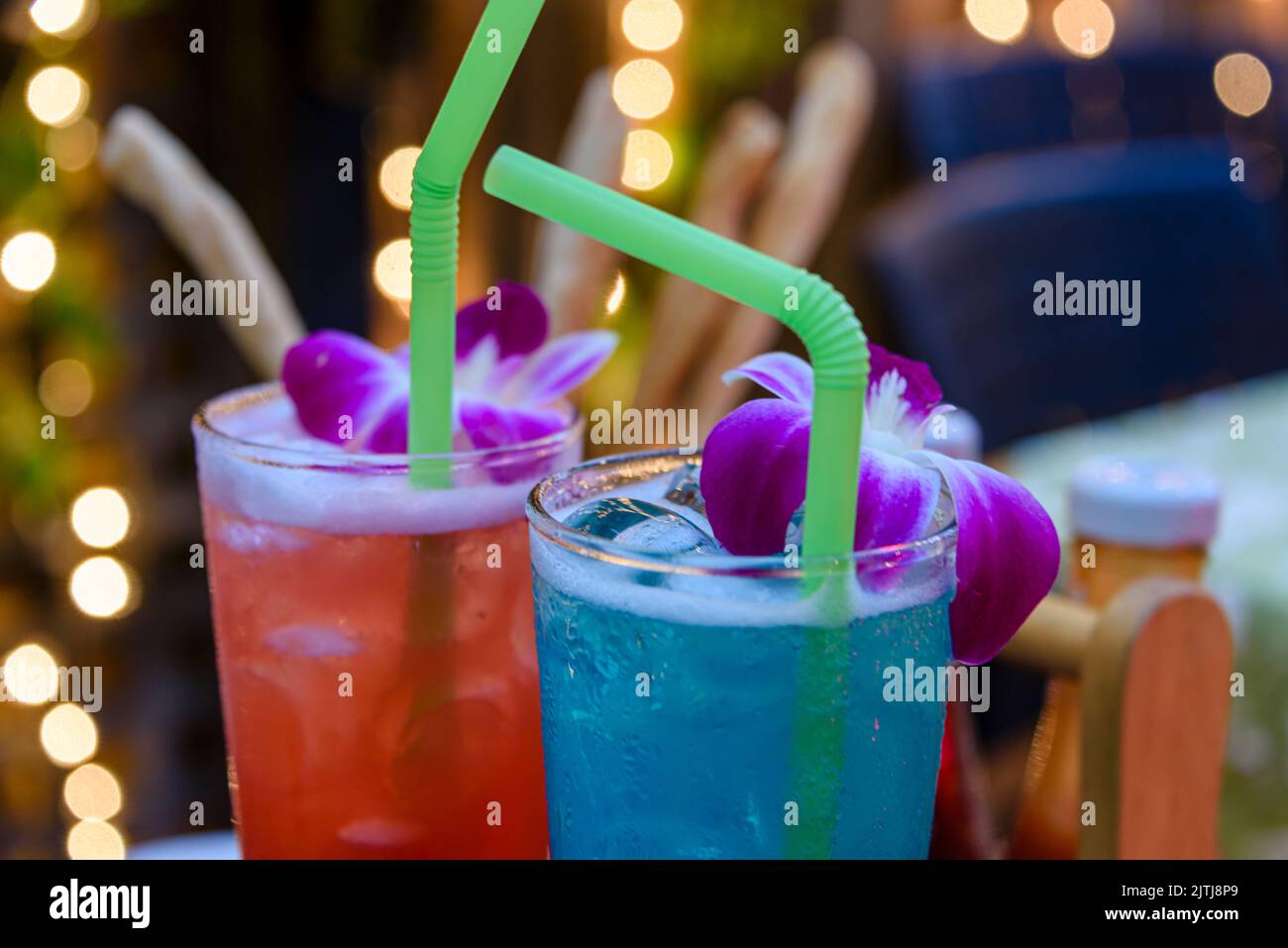 Rote und blaue Cocktails mit Trinkhalmen und violetten Blumen in einer Bar Stockfoto