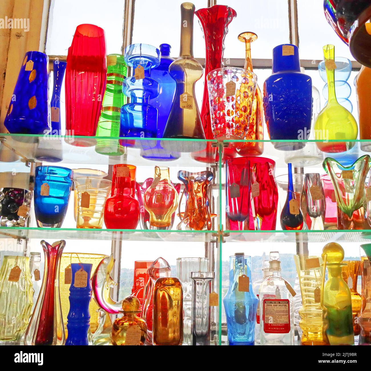 Vintage-bunte gemischte Glaswaren im Fensterregal, beleuchtet Stockfoto
