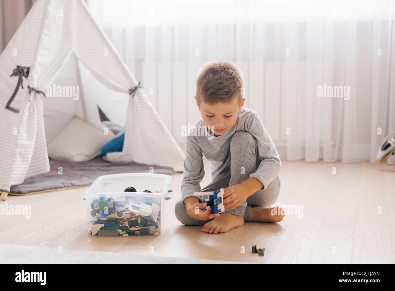 Boy Kind spielt mit Spielzeug, sammelt einen Konstrukteur in einem gemütlichen Kinderzimmer Stockfoto