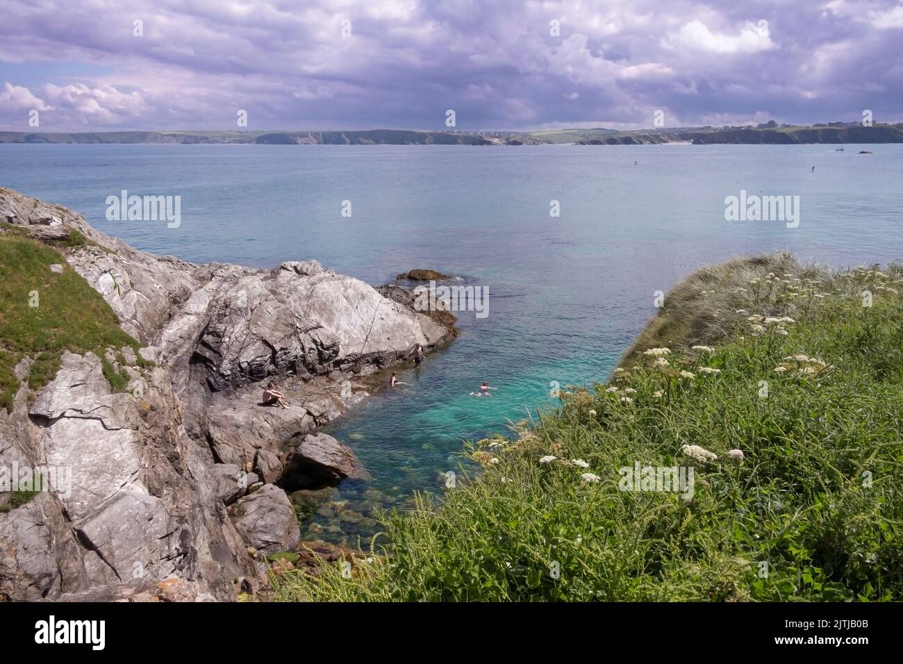 Menschen schwimmen im Meer vor der zerklüfteten Küste von Towan Head in Newquay in Cornwall im Vereinigten Königreich. Stockfoto