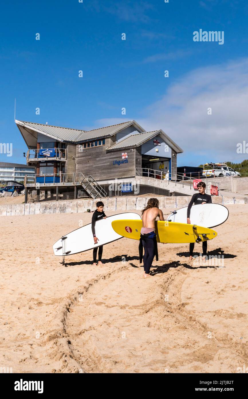 Junge Surfer und ihr Instruktor tragen ihre Surfbretter zu Beginn ihres Surfunterrichts am Fistral Beach in Newquay in Cornwall in England i Stockfoto