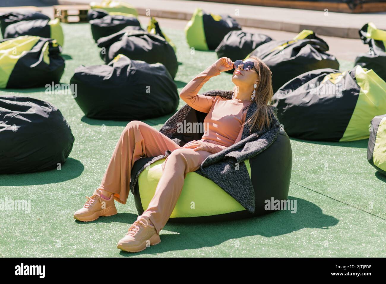 Die hübsche weiße junge Frau liegt auf einem Sessel im Freien, trägt eine Sonnenbrille und lächelt. Das Konzept der Ruhe und Entspannung. Stockfoto