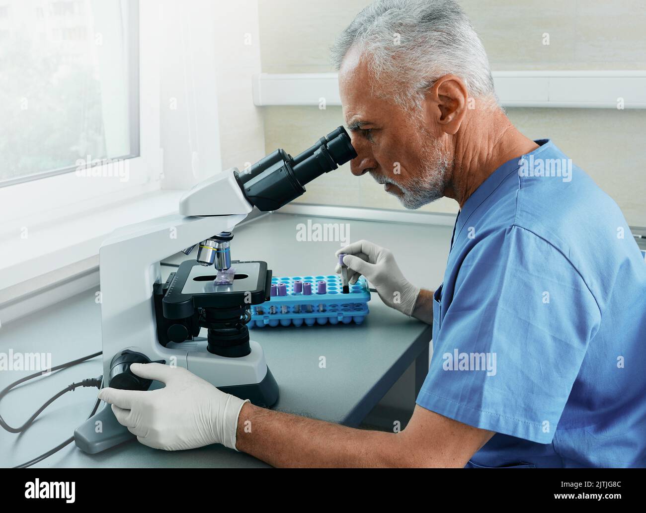 Professioneller männlicher Wissenschaftler, der im Mikroskop arbeitet, während er an der medizinischen Blutforschung im wissenschaftlichen medizinischen Labor arbeitet Stockfoto