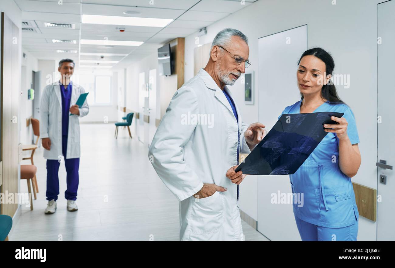 Allgemeinmediziner, der sich mit der Krankenschwester die MRT des Genicks des Patienten ansieht und im Korridorkrankenhaus steht, um eine Erkrankung des Patienten zu diagnostizieren Stockfoto