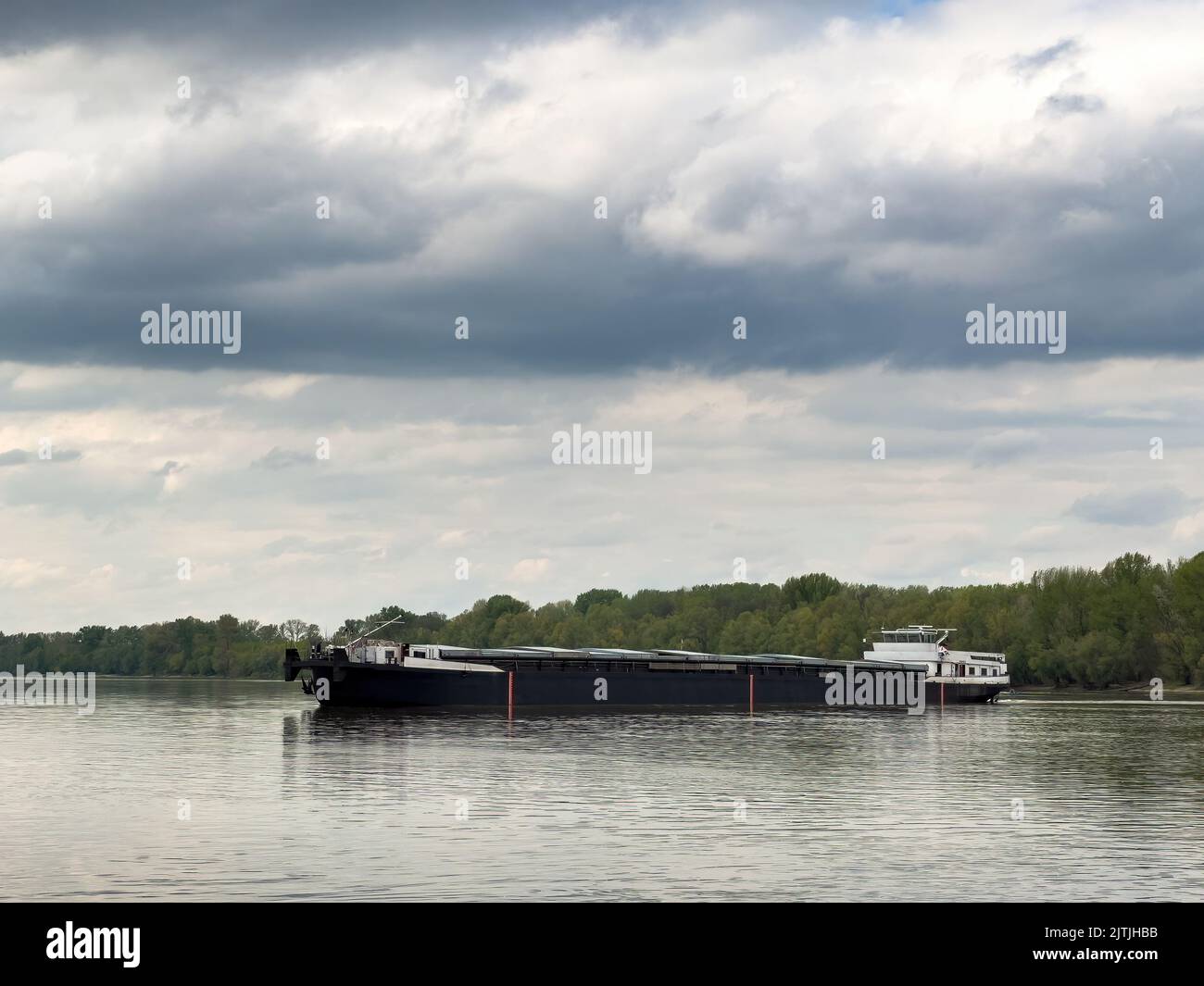 Ein Schiff auf dem Wasser mit grauen Wolken und Bäumen im Hintergrund Stockfoto