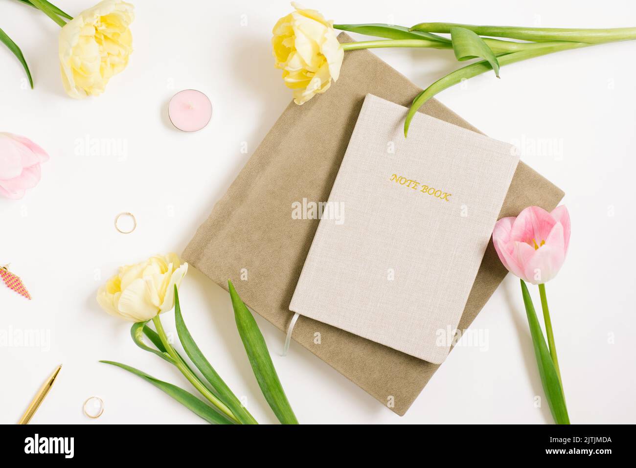 Frauenarbeitsplatz mit Notizbuch, rosa-gelben Tulpenblüten, Stift, Notizbüchern. Das Geschäftskonzept des Bloggers. Flache Position, Draufsicht. Stockfoto