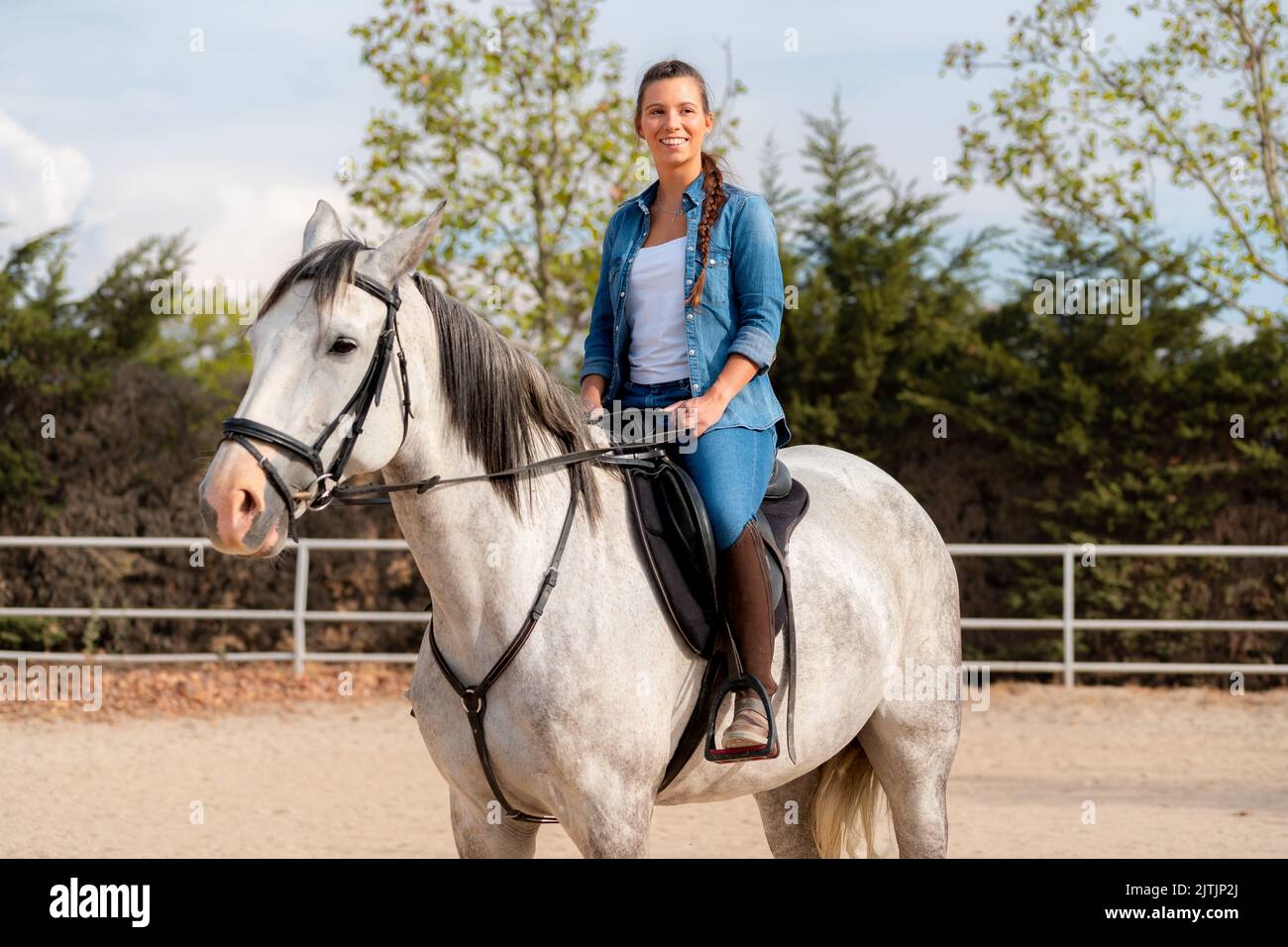 Seitenansicht einer Frau, die im Sommer auf einem weißen Pferd in einem Stall posiert Stockfoto