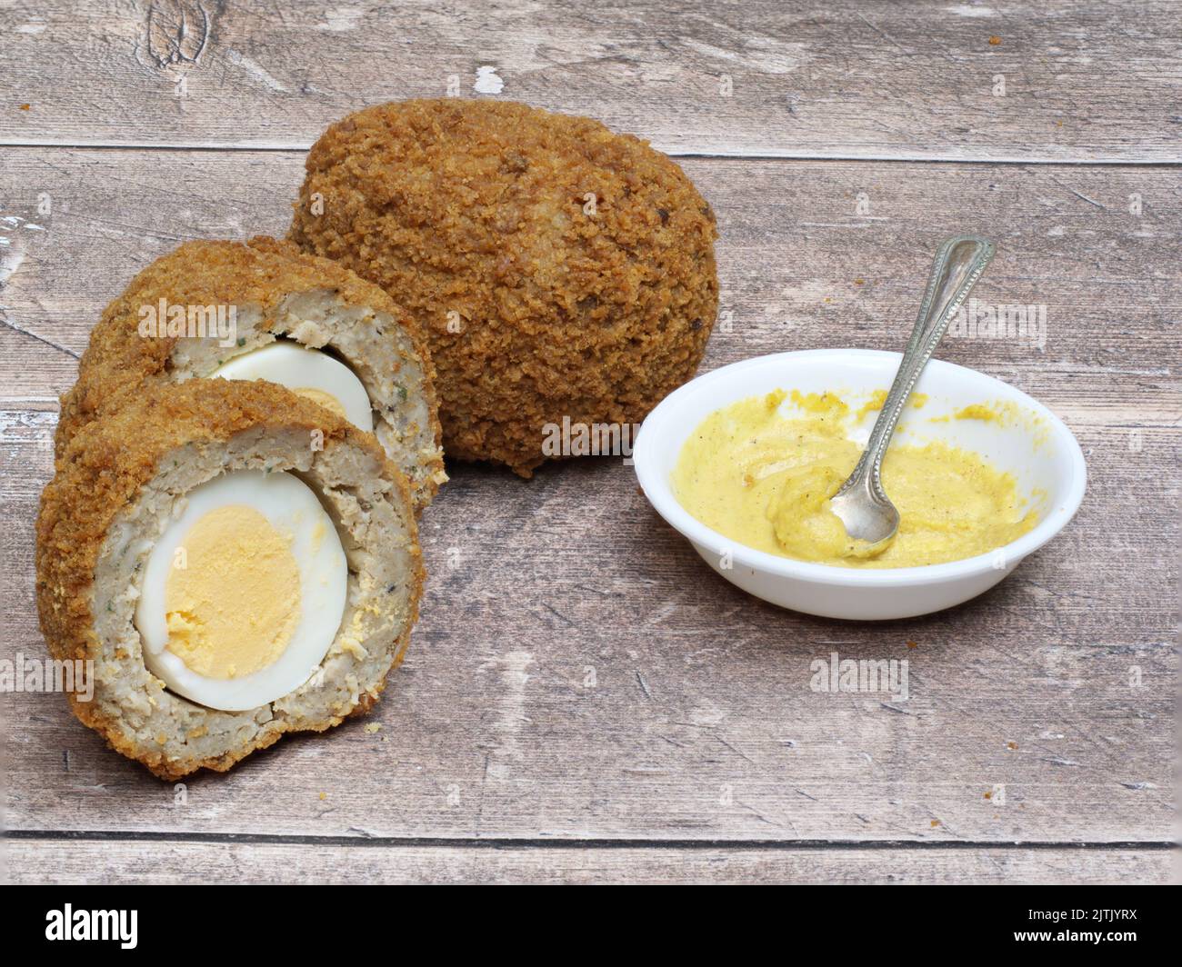 Schottische Eier halbierten sich auf einem Holztisch mit englischem Senf in einer weißen Schüssel und Löffel Stockfoto