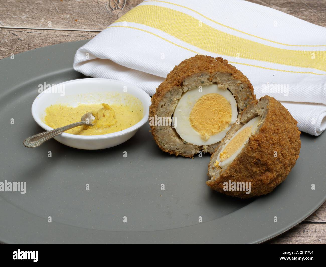 Single Scotch Egg halbiert auf einem Teller mit englischem Senf in einer weißen Schüssel und Löffel Stockfoto