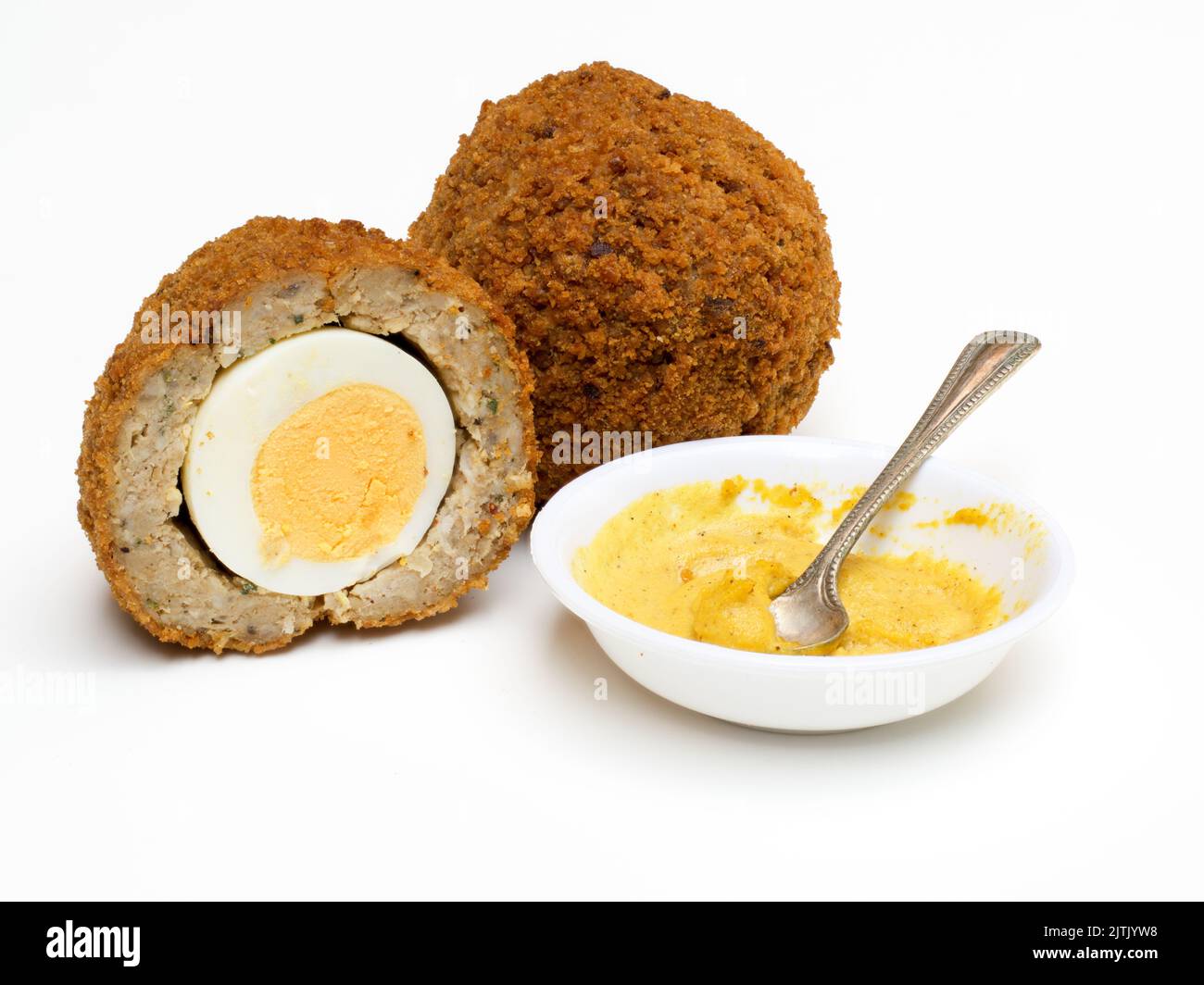 Scotch Eier halbierte man isoliert auf weißem Hintergrund mit englischem Senf in einer weißen Schüssel und Löffel Stockfoto