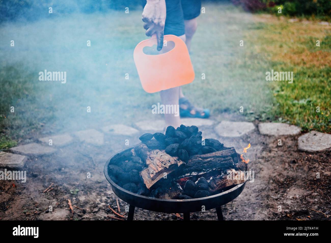 So verwenden Sie einen Holzkohlegrill. Mann mit Kunststoff BBQ Handventilator in der Nähe von Holzkohle Grill Feuer. Grill Kunststoff BBQ Handventilator Stockfoto