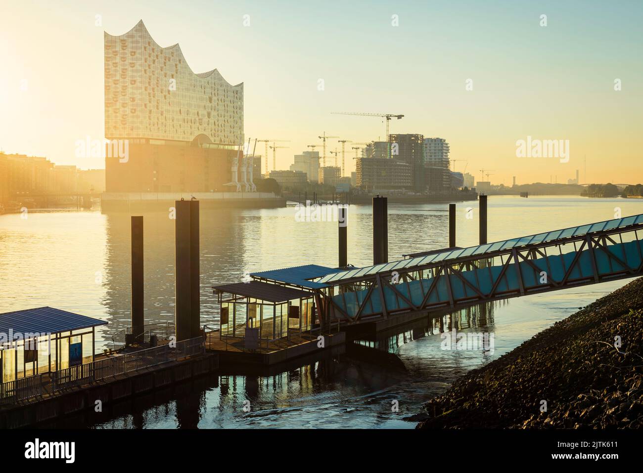 Sonnenaufgang an der Elbphilharmonie, HafenCity und eine Fähranlegestelle an der Elbe im Hamburger Hafen Stockfoto