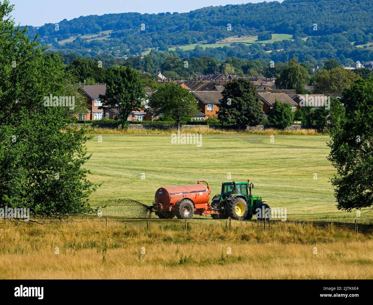 Landwirt arbeiten Fahren Traktor & zylindrischen Düngebehälter Sprühen Entleerungs Gülle auf Land Ackerland Weide Gras - Yorkshire, England Großbritannien Stockfoto