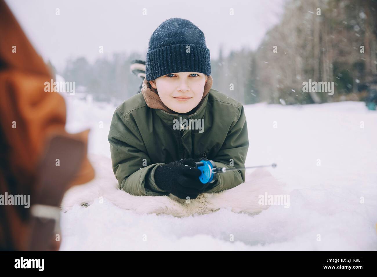 Porträt eines lächelnden Jungen im Strick, der auf dem Schnee liegt Stockfoto