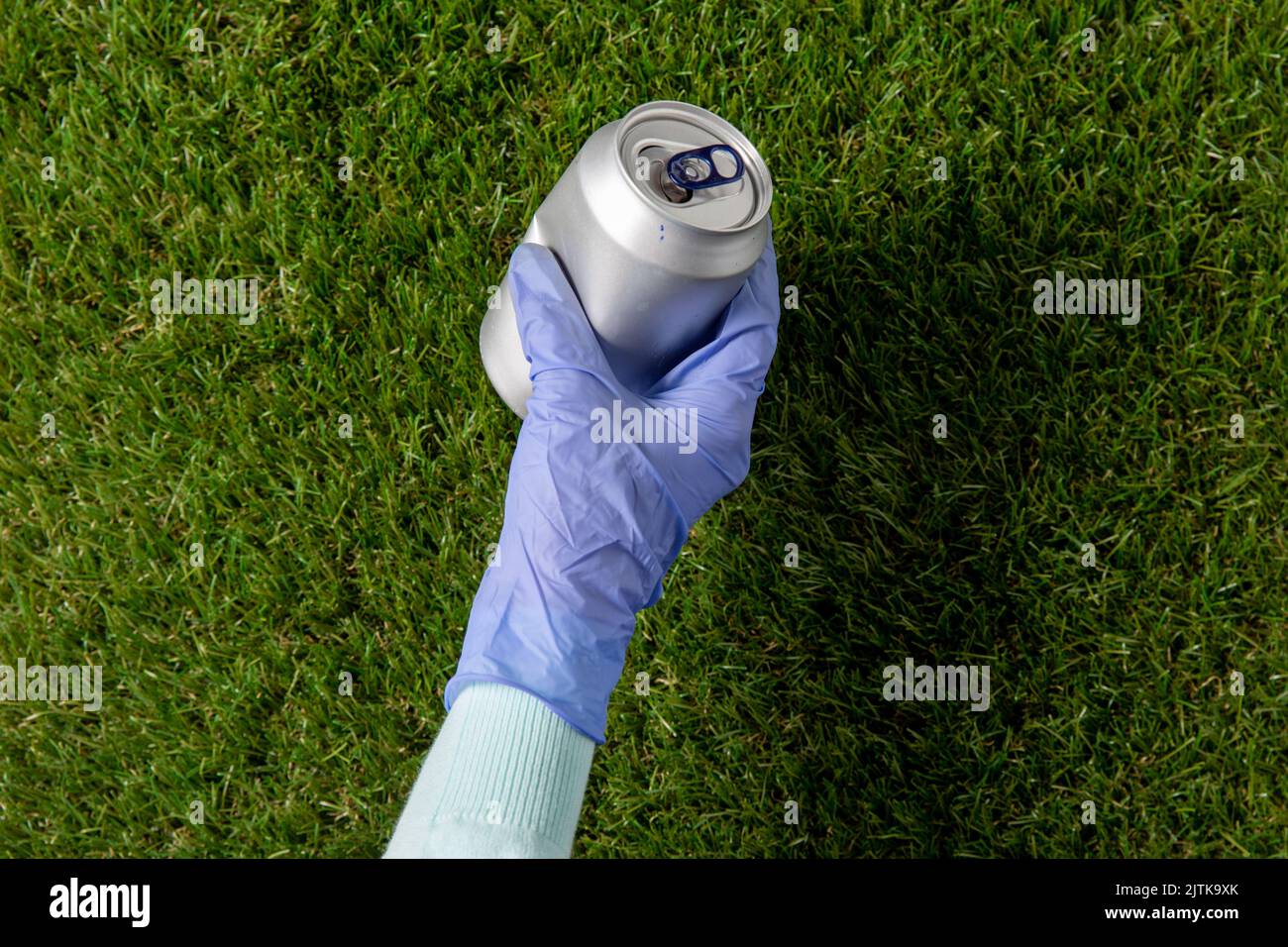 Nahaufnahme der Hand im Handschuh mit gebrauchter Dose auf Gras Stockfoto
