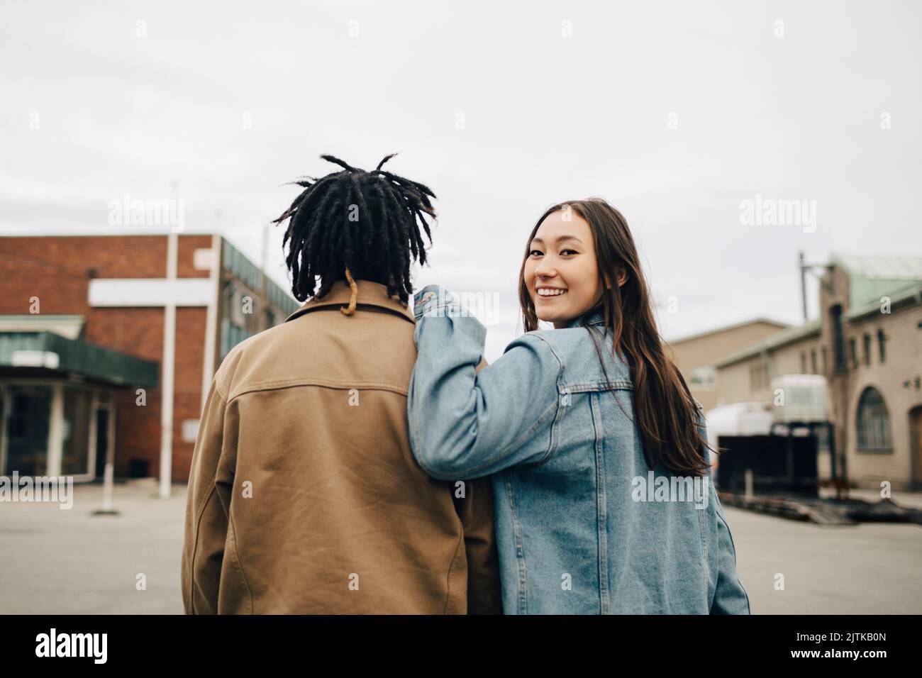 Lächelnde Frau, die über die Schulter schaut, während sie mit einem Freund auf der Straße läuft Stockfoto