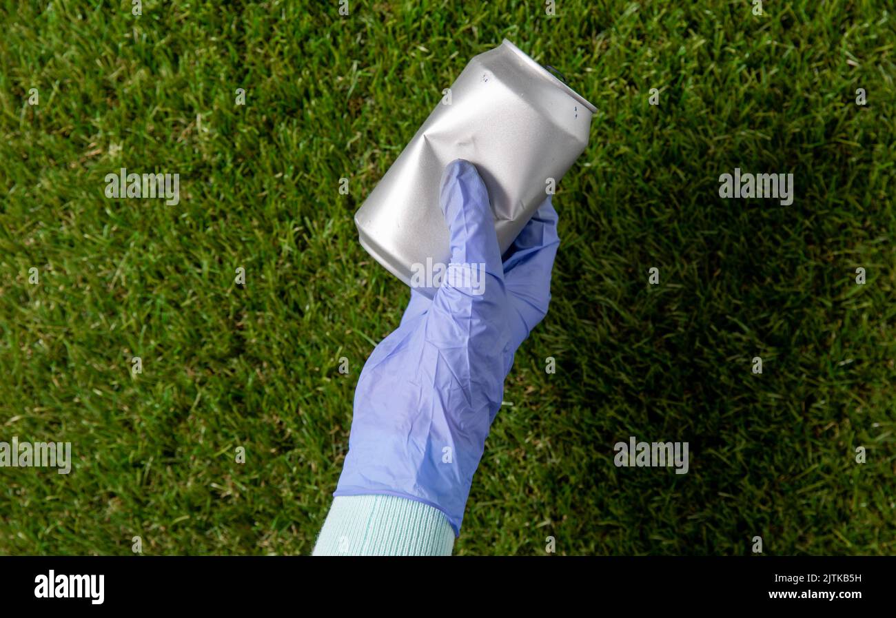 Nahaufnahme der Hand im Handschuh mit gebrauchter Dose auf Gras Stockfoto
