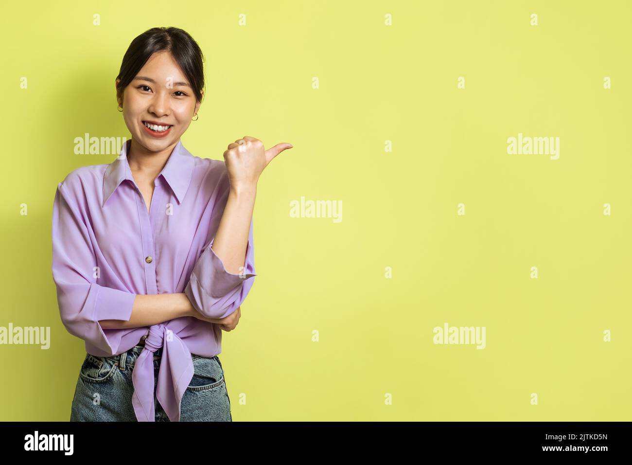 Japanische Dame Zeigt Daumen Finger Beiseite Werbeangebot, Gelber Hintergrund Stockfoto