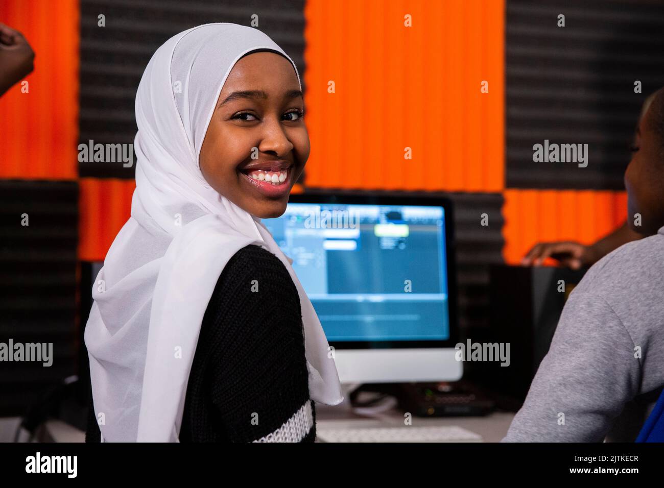 Portrait eines lächelnden Mädchens mit Hijab, das im Aufnahmestudio sitzt Stockfoto