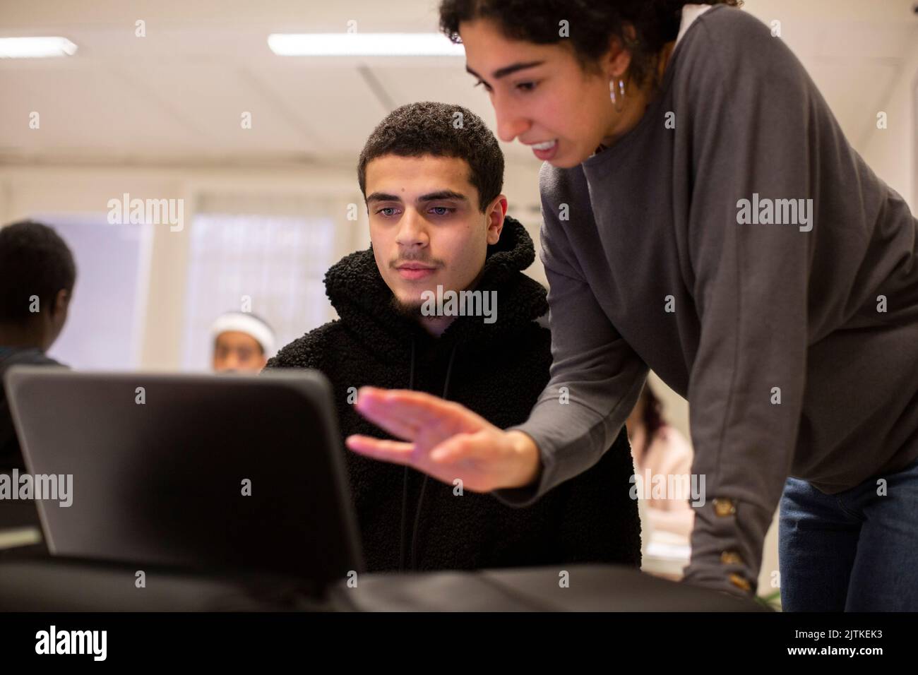 Der Schüler schaut auf den Laptop, während der Lehrer im Klassenzimmer erklärt Stockfoto