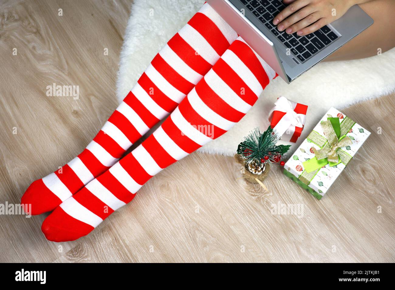 Mädchen in Weihnachtskniesocken sitzen auf einem Pelzteppich mit Laptop in der Nähe der Geschenkboxen. Bestellung von Geschenken, Arbeit und Freizeit zu Hause während der Neujahrsferien Stockfoto