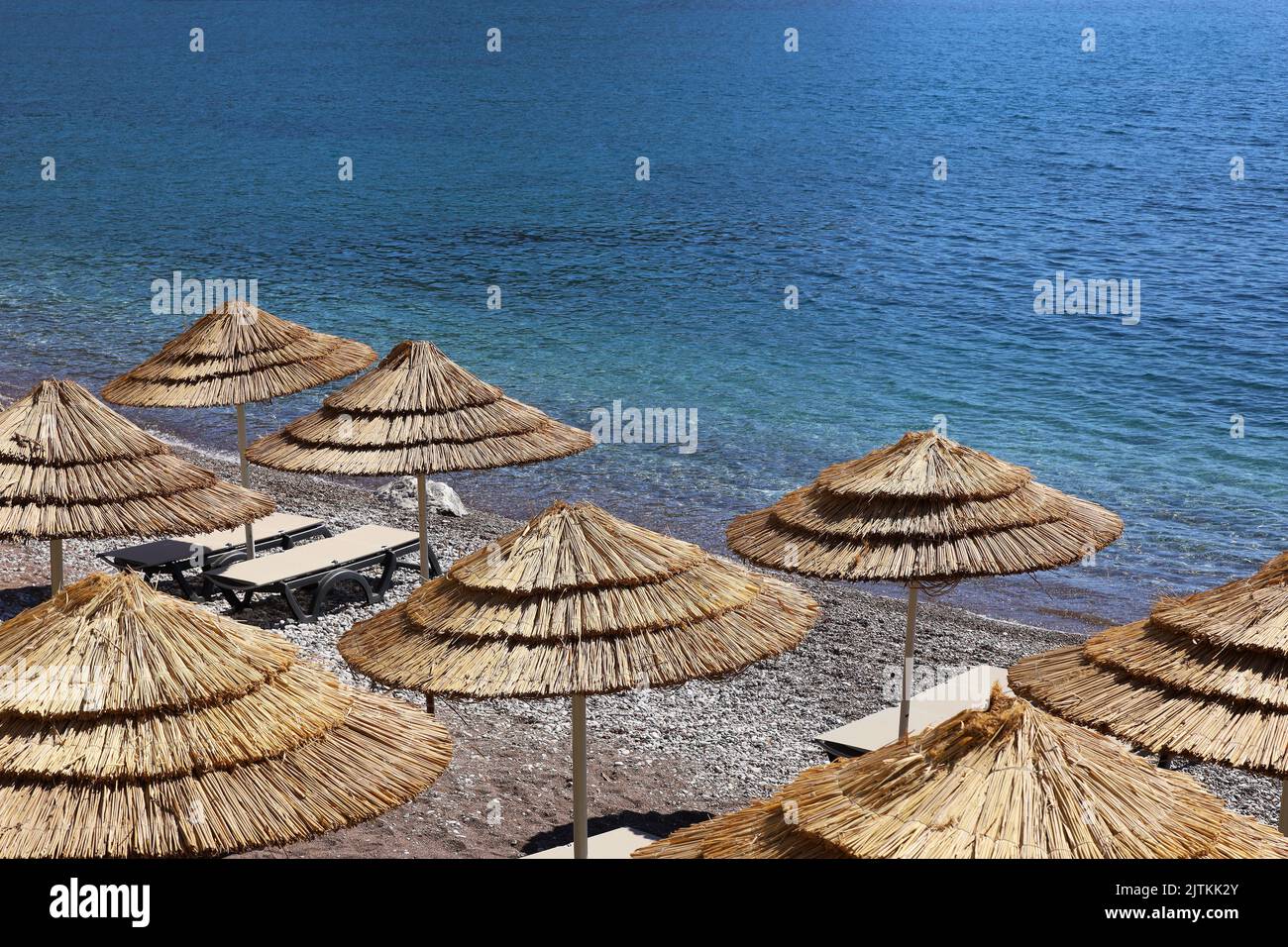 Leerer Kiesstrand mit Korbschirmen und Liegestühlen. Malerischer Blick auf das Meer mit blauem Wasser, Sommerresort Stockfoto