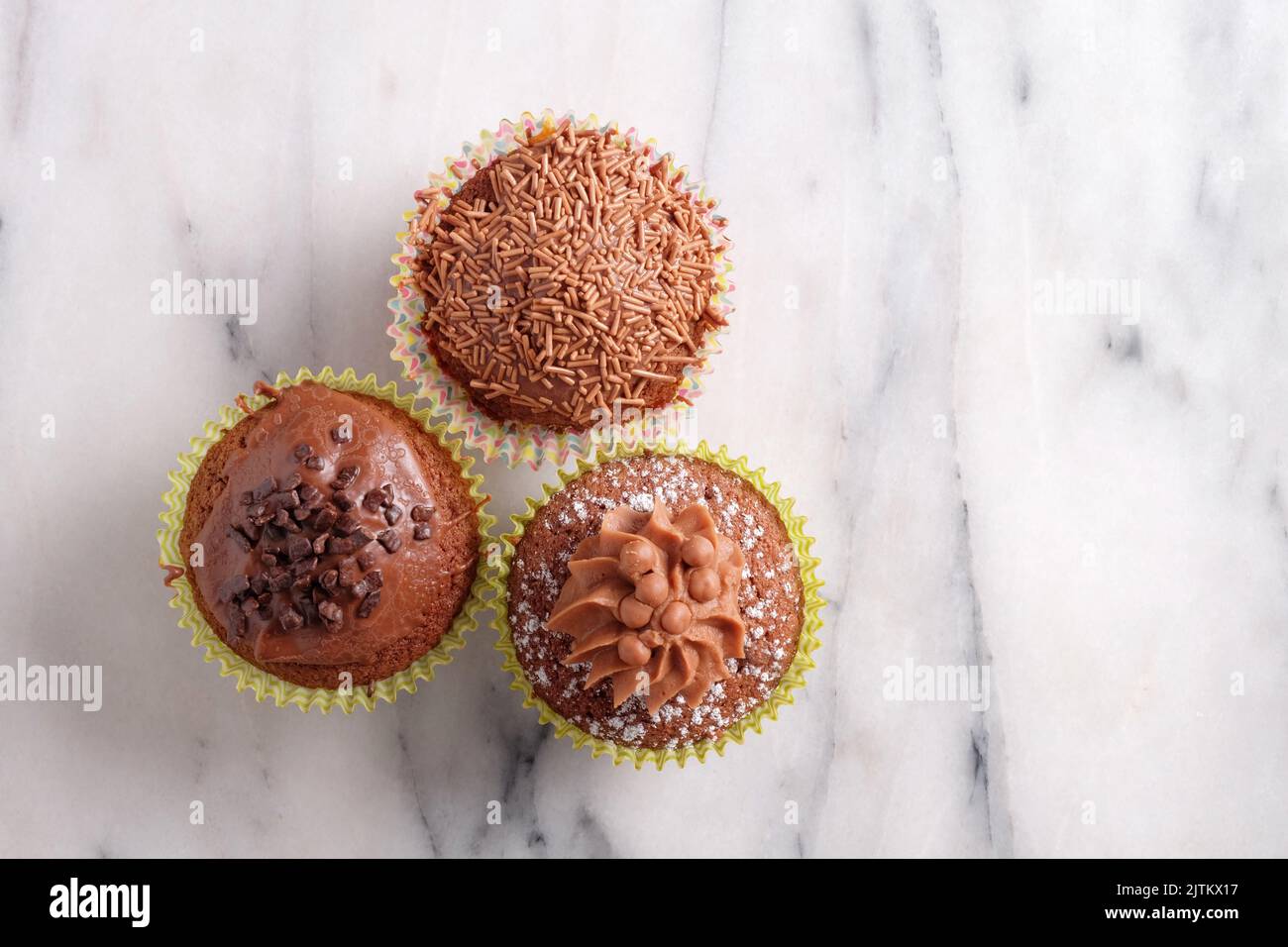Drei verschiedene Cupcakes aus Schokolade, die von oben auf grauem Marmorboden mit Kopierfläche geschossen wurden Stockfoto