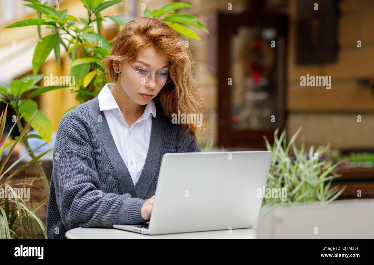 Junge, konzentrierte Frau, die im Café im Freien am Laptop arbeitet Stockfoto