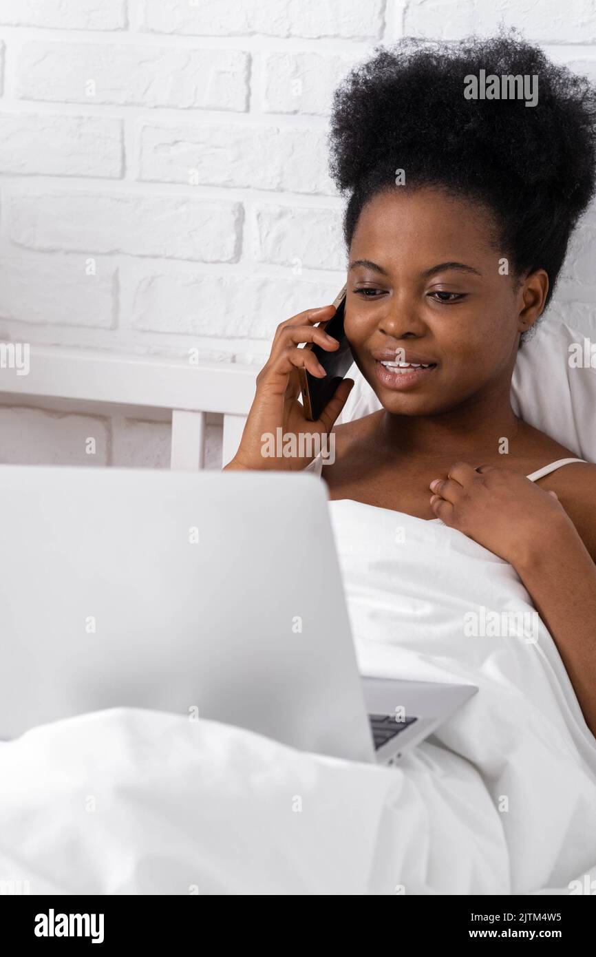Glücklich attraktive afroamerikanische Mädchen arbeiten Büro aus der Ferne, Schwarze Frau mit Laptop-Computer und Telefon sitzen im Bett zu Hause, Distanz Stockfoto