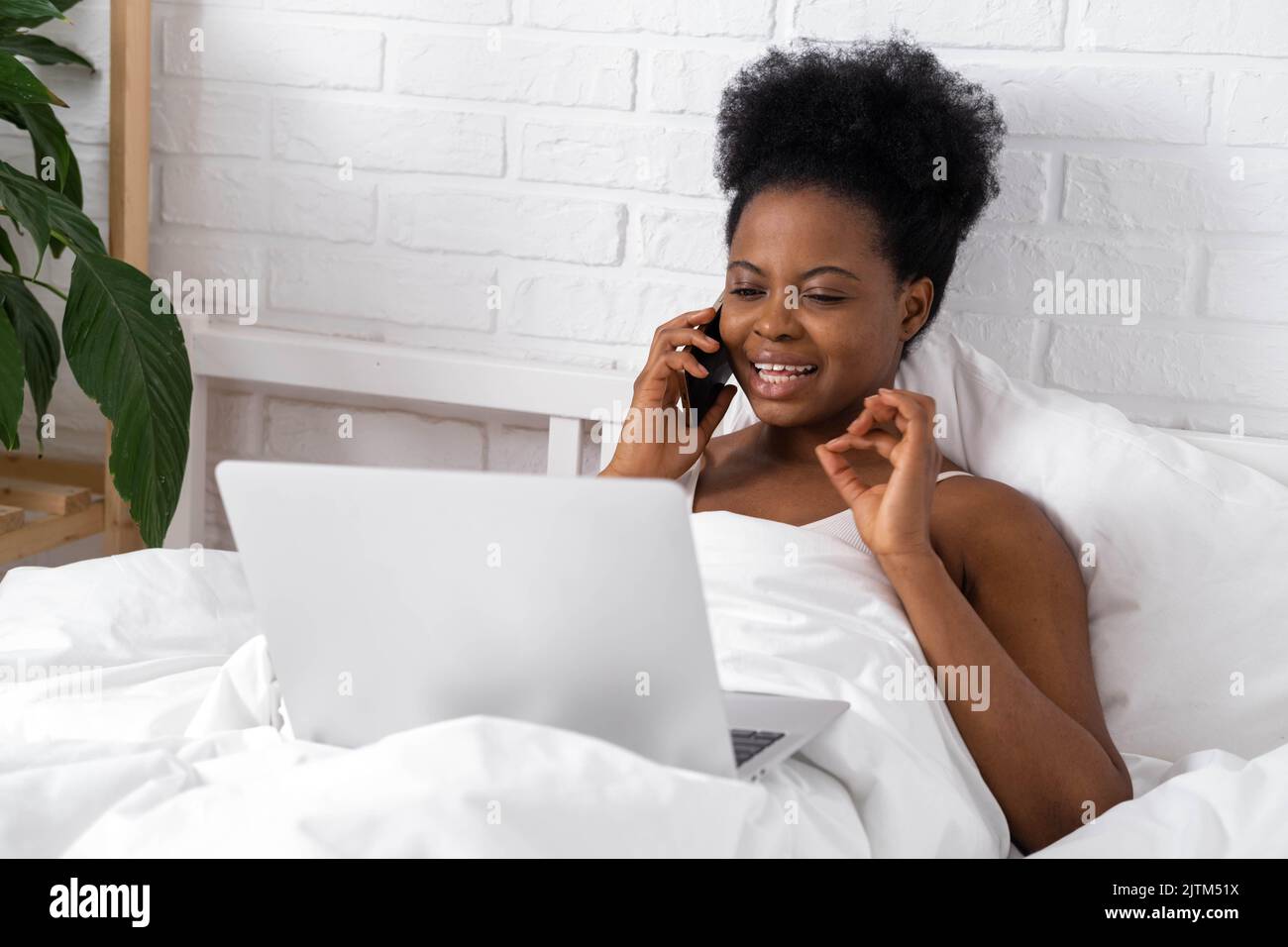 Glücklich attraktive afroamerikanische Mädchen arbeiten Büro aus der Ferne, Schwarze Frau mit Laptop-Computer und Telefon sitzen im Bett zu Hause, Distanz Stockfoto
