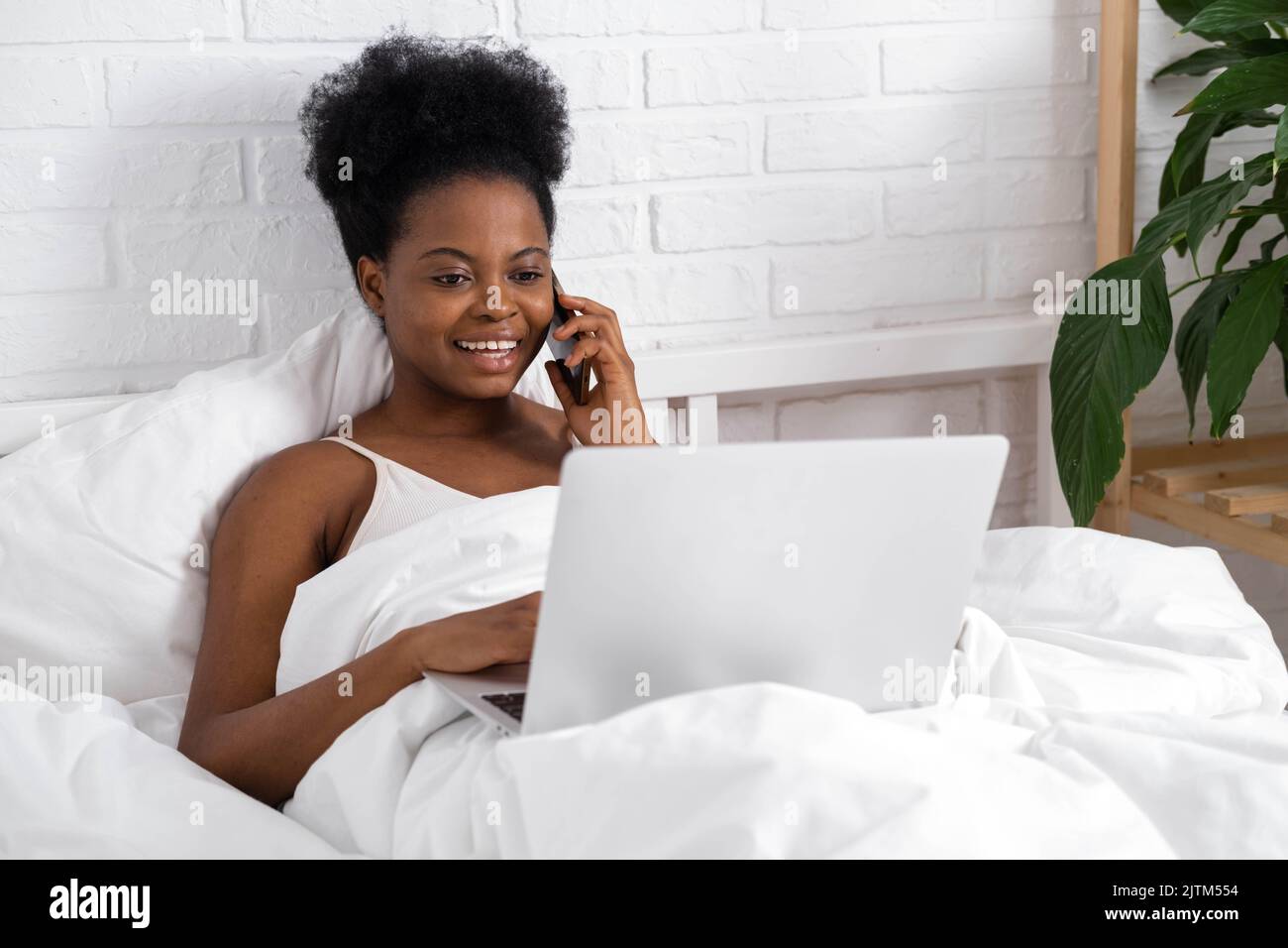 Glücklich attraktive afroamerikanische Mädchen arbeiten Büro aus der Ferne, Schwarze Frau mit Laptop-Computer und Telefon sitzen im Bett zu Hause, Distanz Stockfoto